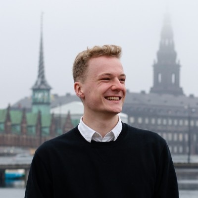 Portrait photo of CS2 skin trader Alkem1st smiling outdoors with a European city skyline in the background
